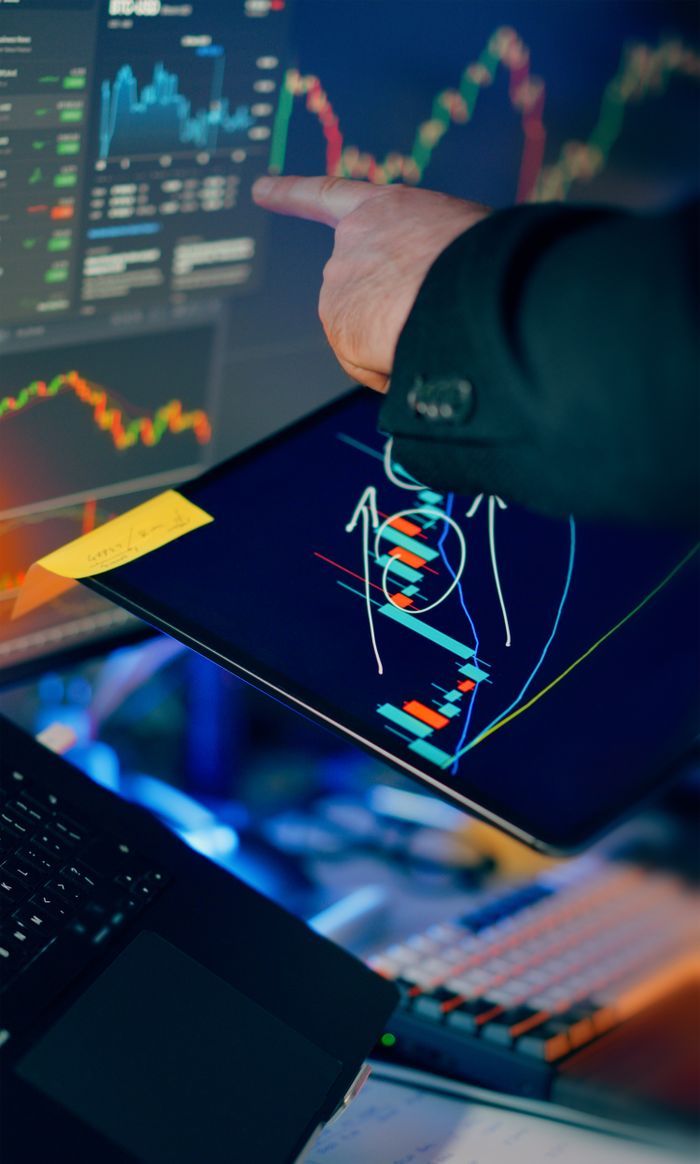 Home A business professional examines financial charts on a tablet and monitor for investment strategy.